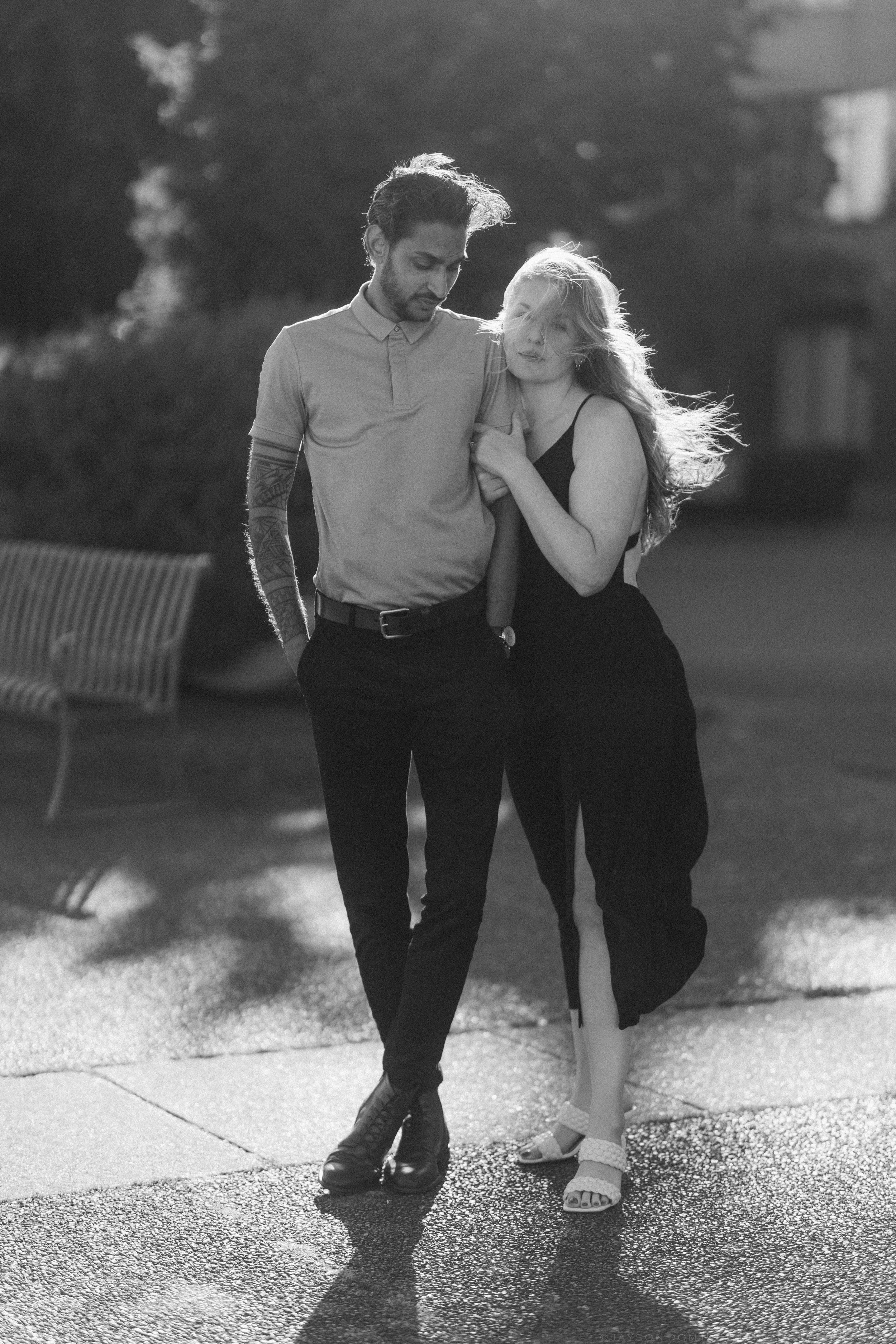 Black and white photo of a couple walking together outdoors, woman leaning on mans shoulder affectionately.