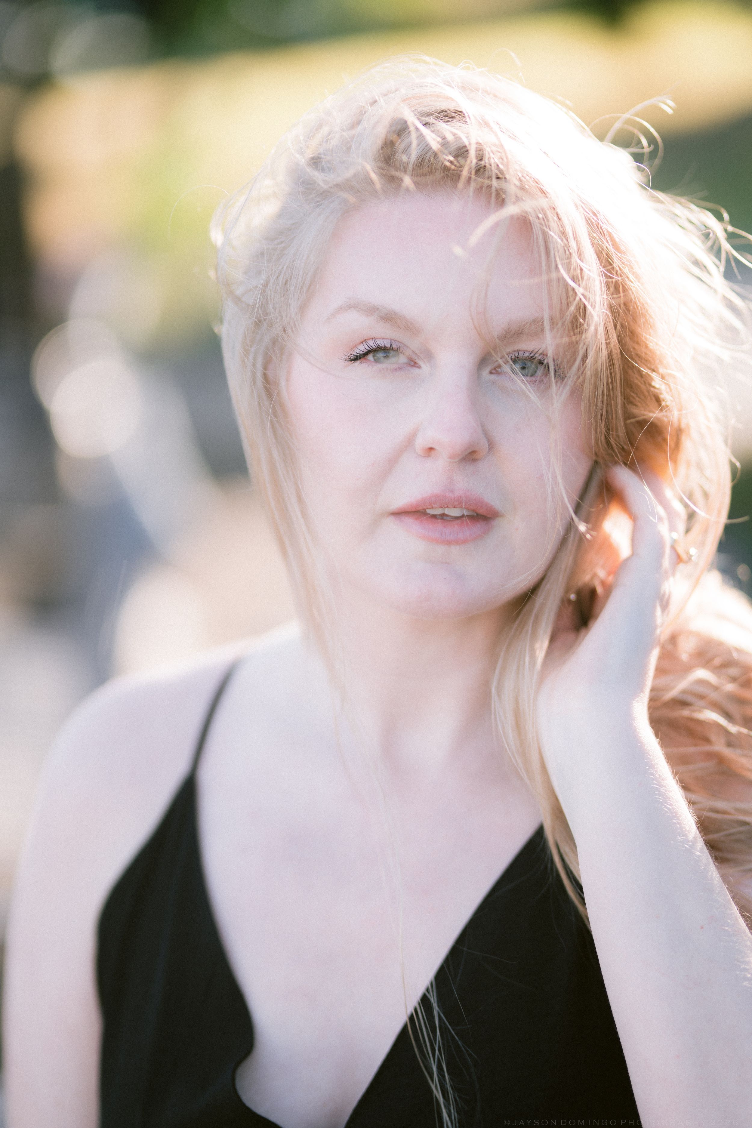 Close portrait of blonde woman in black top with windswept hair in soft natural sunlight outdoors.