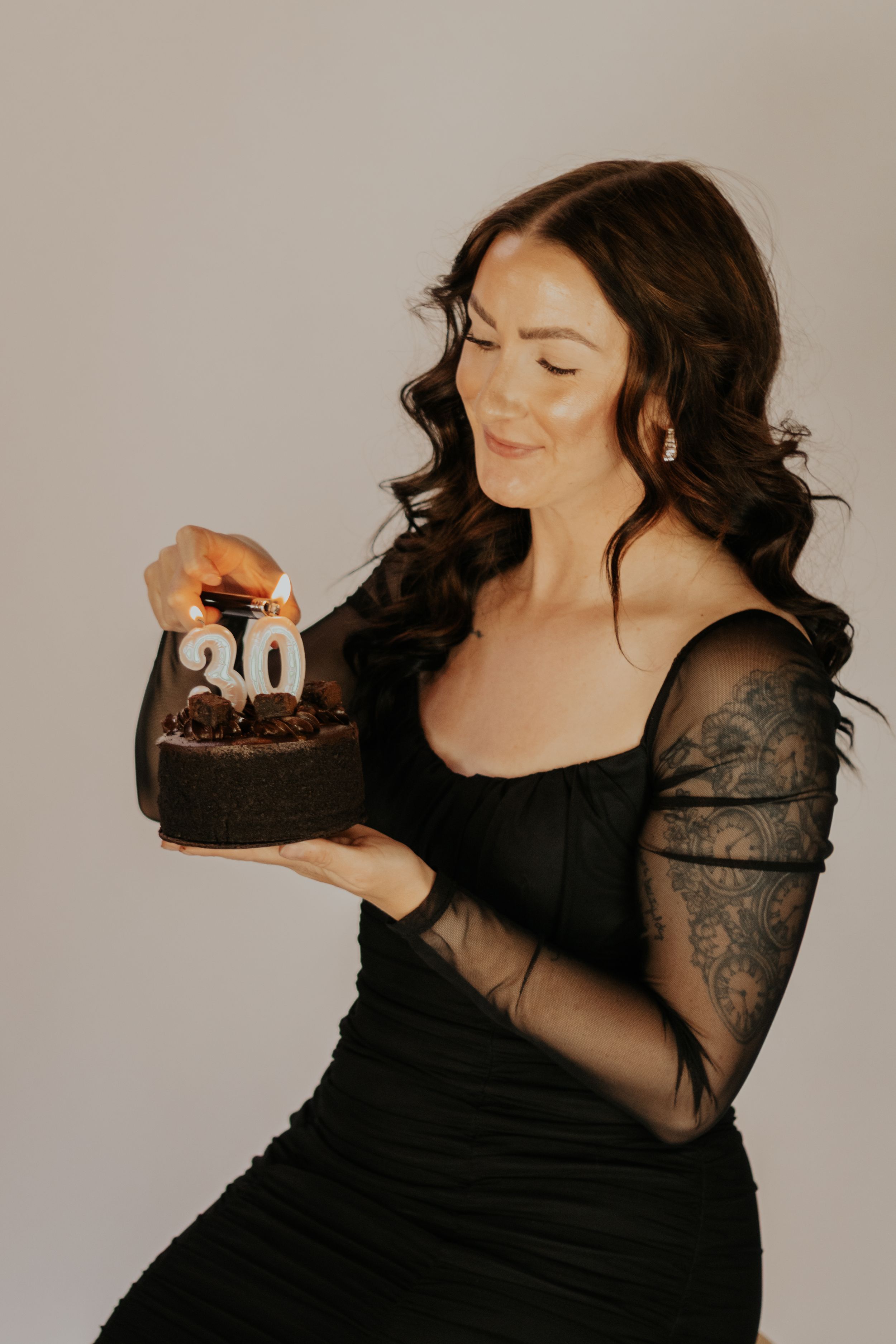 Woman in black lace dress lighting candles on a chocolate birthday cake with number 30 candles.