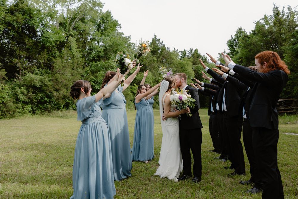 Bridal party forms arch with bouquets as bride and groom walk through at outdoor wedding ceremony.