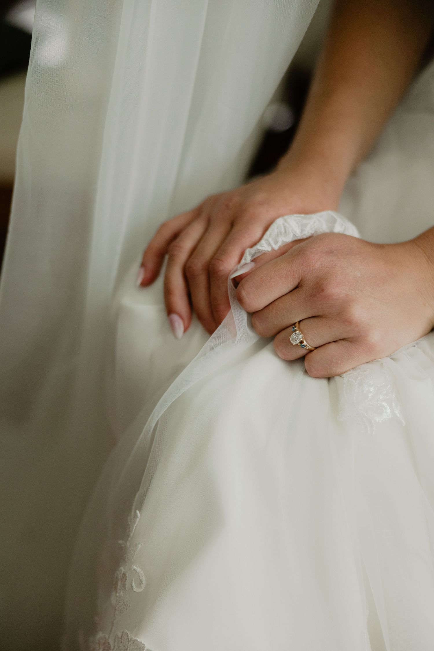 Close-up of bride's hands holding white tulle wedding dress with diamond engagement ring.