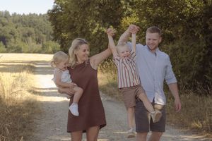 Glückliche Familie mit zwei Kindern bei einem natürlichen Familienshooting auf einem sonnigen Feldweg im Aargau.