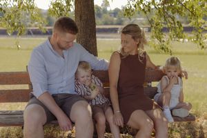 Glückliche Familie mit zwei Kindern bei einem natürlichen Familienshooting auf einem sonnigen Feldweg im Aargau.