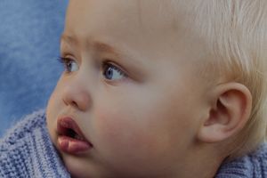 Close-up portrait of a blonde toddler with blue eyes gazing upward, wearing a blue knit sweater.