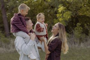 Happy young family with two toddlers laughing together in a lush green park during autumn.