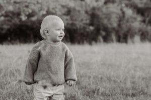 Black and white photo of a happy toddler in a knit sweater standing in a grassy field.