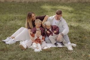 A happy family with two young children sits together on a blanket in a green field during an outdoor photo session.