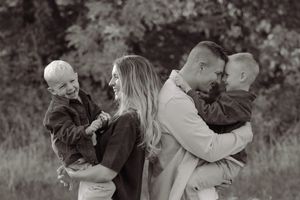 Black and white family photo of parents holding two young boys outdoors, smiling and laughing together.
