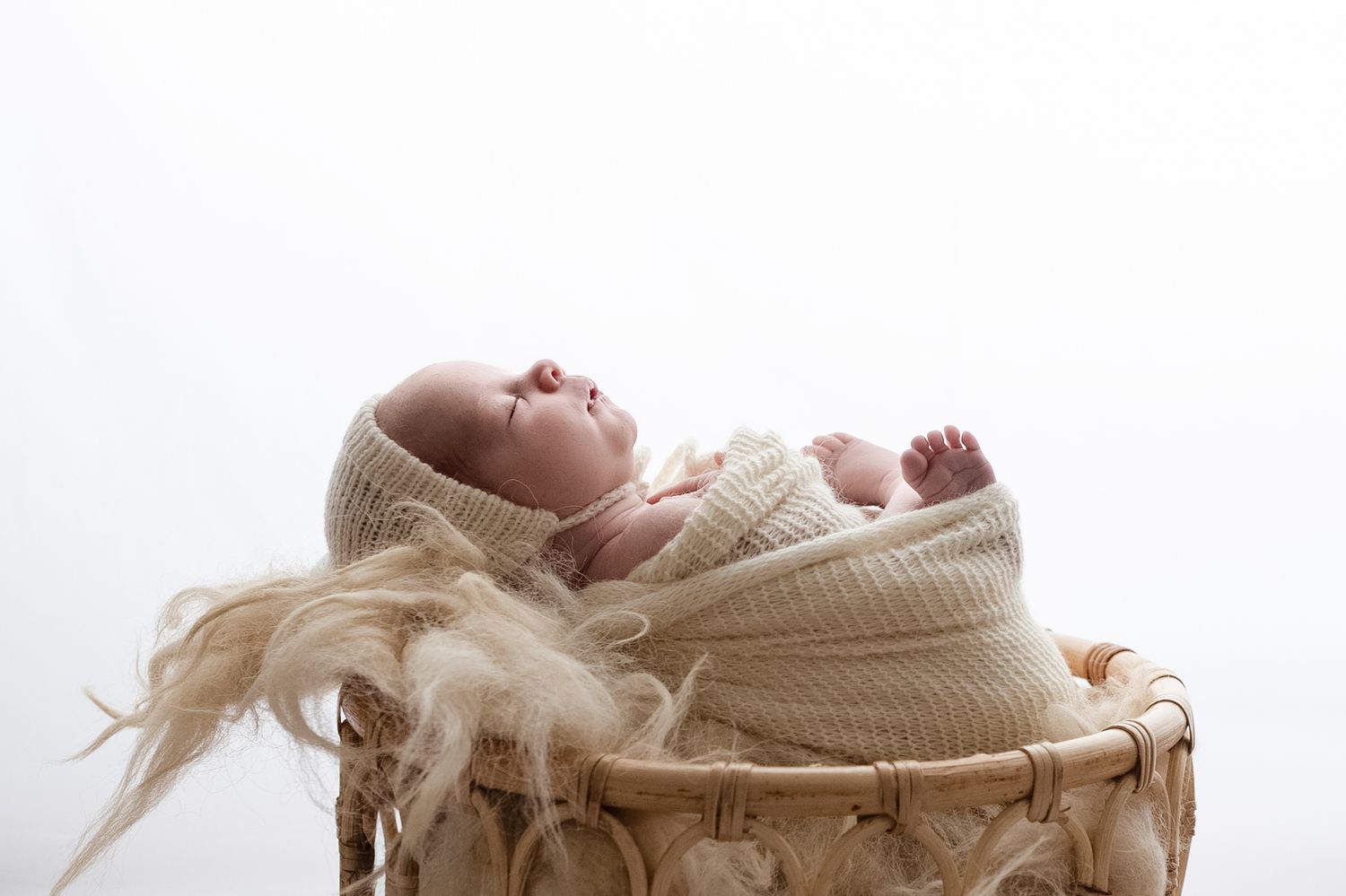 Backlit baby sleeps wrapped in cream knits in a boho basket and on soft wool, captured by Charlottesville newborn photographer.