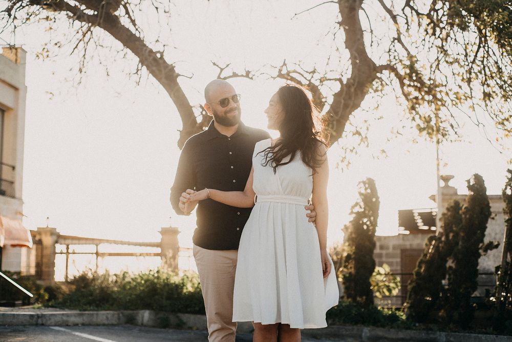 A couple shares a romantic moment outdoors, with golden sunlight filtering through trees as they smile at each other.