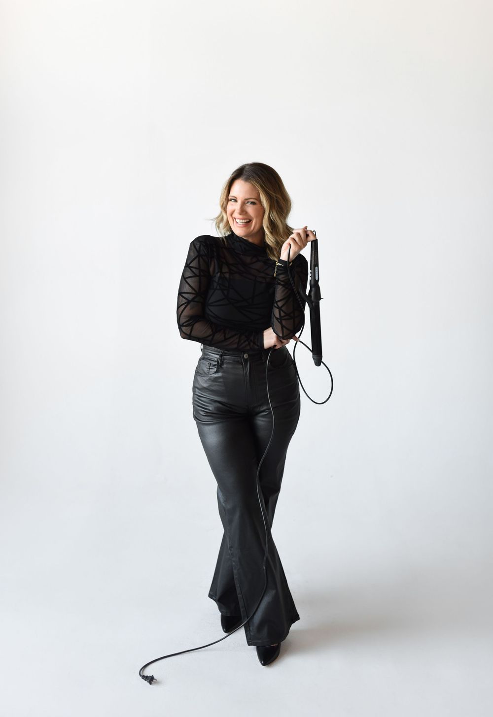 A hairstylist standing holding a curling iron during a branding session in a natural light studio.