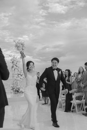 Joyful newlyweds celebrating recessional walk down the aisle, bride raising bouquet triumphantly.