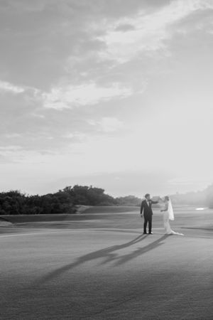 Bride and groom sharing a romantic moment on an open golf course at sunset with long shadows.