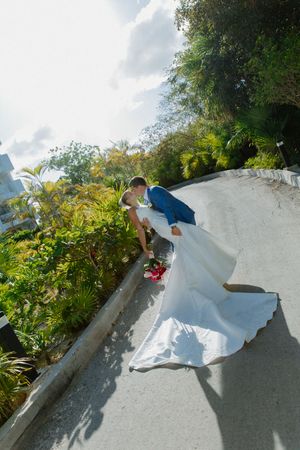 Bride and groom sharing a romantic dip kiss on a curved pathway surrounded by lush tropical greenery.
