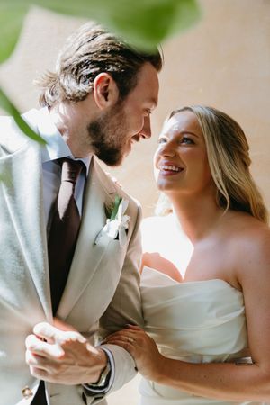 Smiling bride and bearded groom in a tan suit share a tender close moment at their outdoor wedding ceremony.