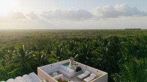 Aerial view of a rooftop pool surrounded by lush tropical jungle and palm trees at sunset.