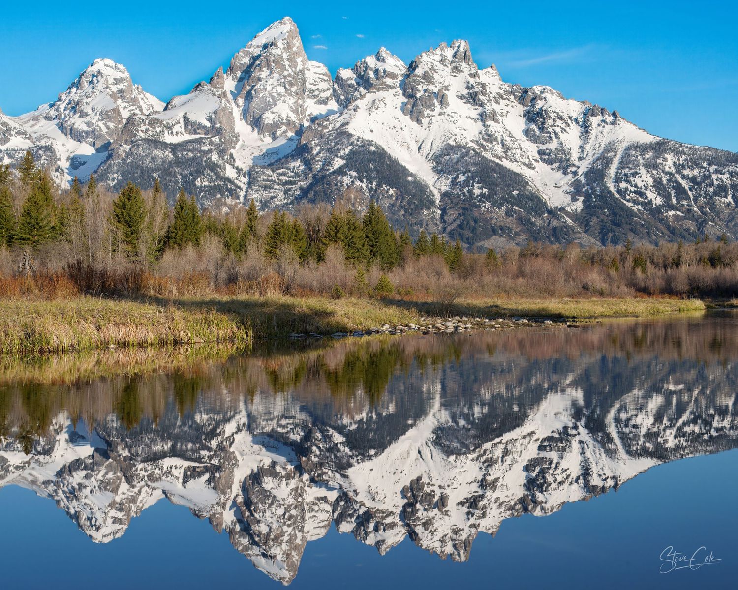 Snow-capped Teton mountain peaks perfectly reflecting in calm water on a clear day, fine art landscape photo by Steve Cole.