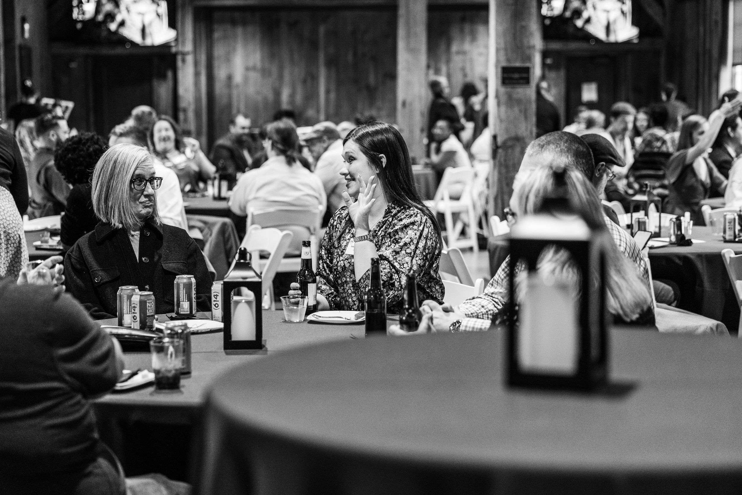 Black and white photo of women laughing and socializing at a formal banquet event with round tables.