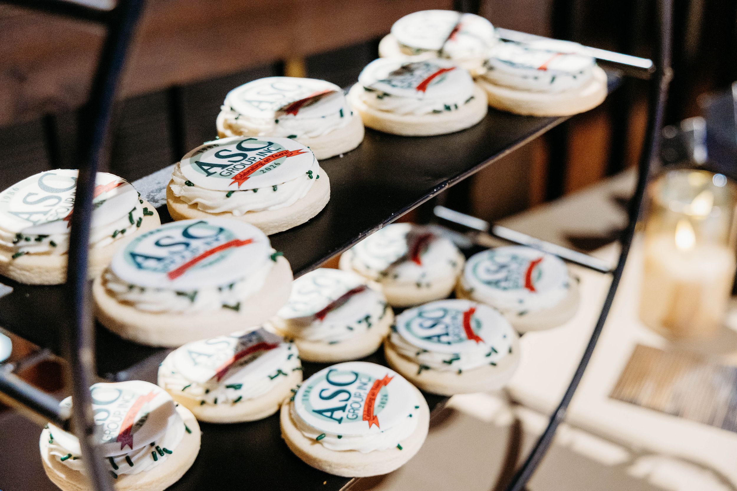 Round frosted cookies decorated with ASC logo displayed on a tiered metal rack at a catered event.