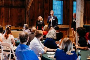 Speakers present to an engaged audience in a rustic barn venue during a professional networking event.