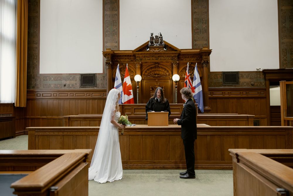 Bride and groom exchange vows before officiant in elegant wood-paneled courthouse courtroom ceremony.