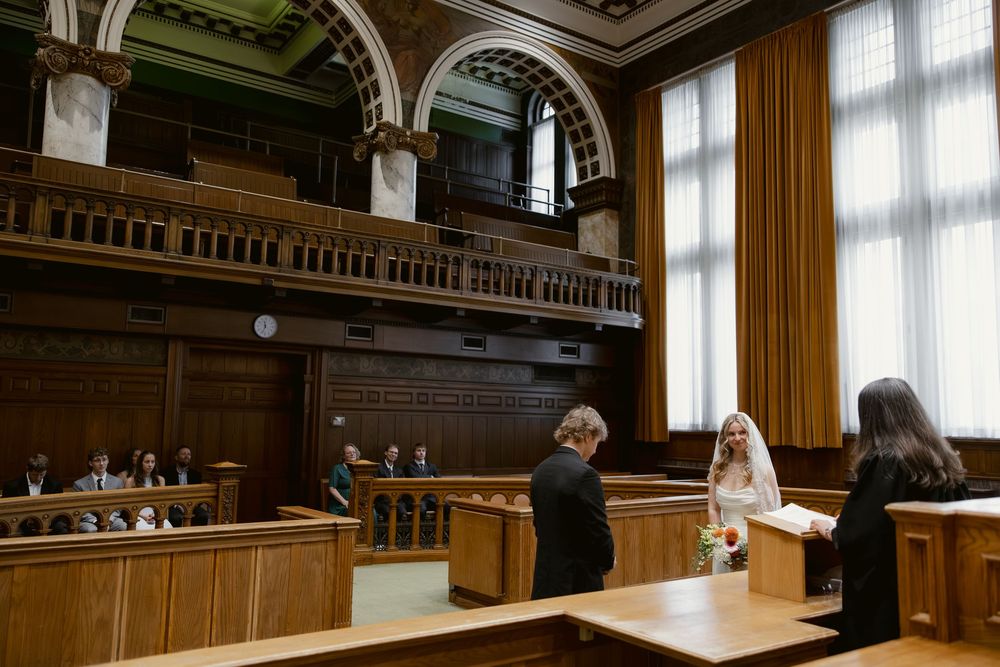 Bride and groom stand at podium during intimate courthouse wedding ceremony in grand historic courtroom.
