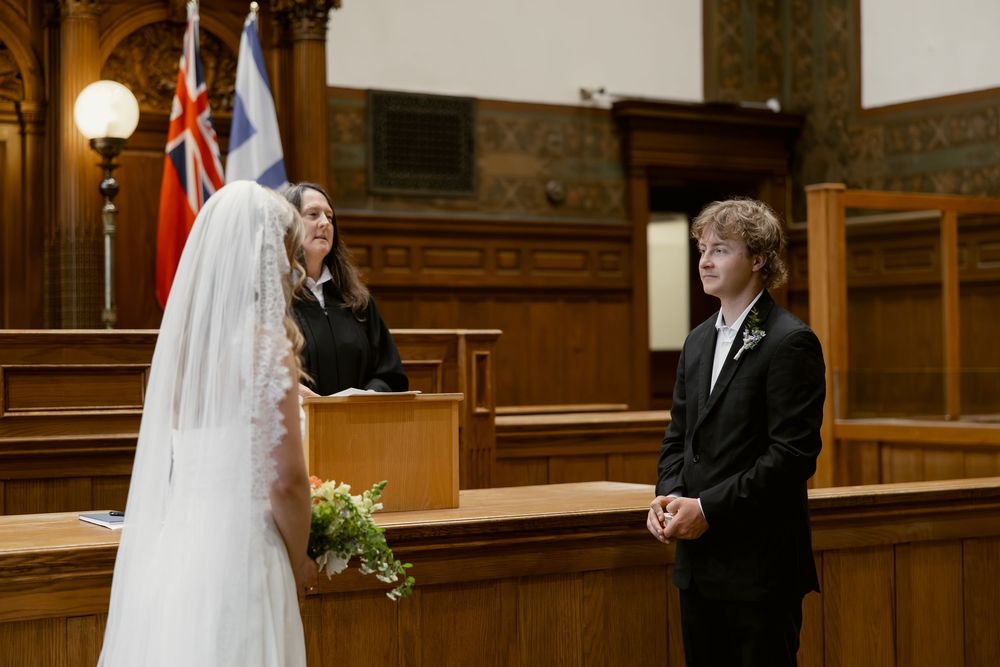 Bride and groom face each other smiling during intimate courthouse wedding ceremony with officiant behind.