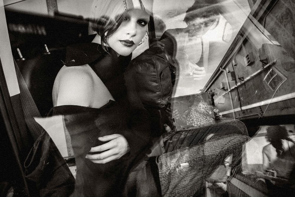 Black and white photo of a glamorous woman in dark clothing reflected in a glass window at night.
