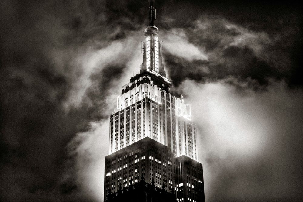 Dramatic black and white photo of the Empire State Building shrouded in dark storm clouds at night.