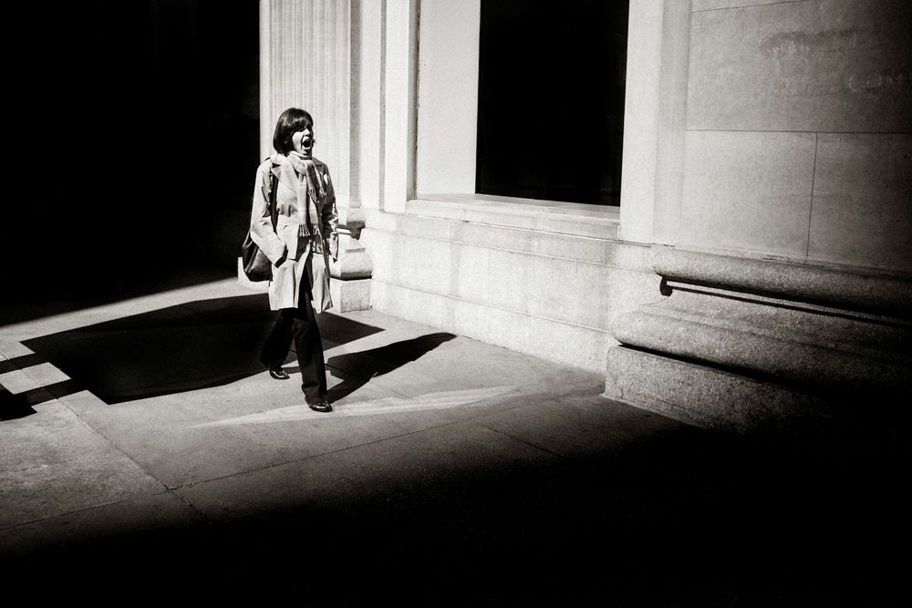 Black and white photo of a woman standing in sunlight between large stone columns of a classical building.