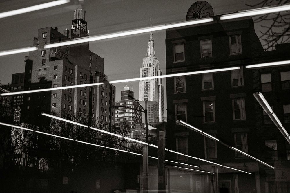 Black and white NYC skyline with Empire State Building reflected in glass with neon light streaks.