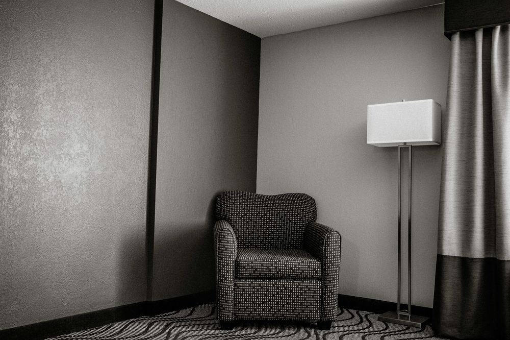 Elegant hotel room corner with a patterned armchair, tall floor lamp, and gray walls on a geometric carpet.