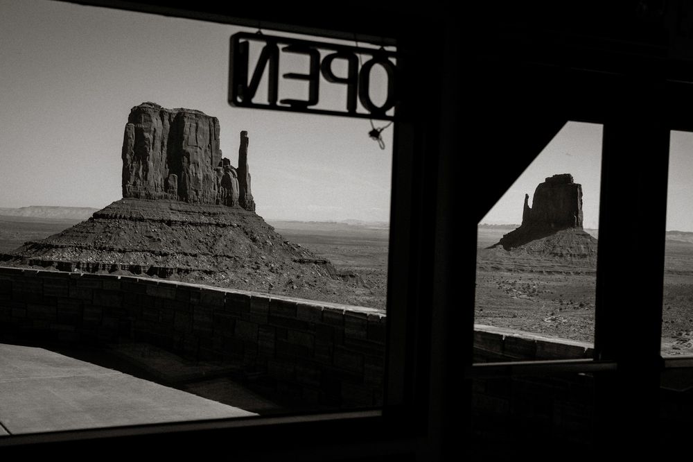 Black and white photo of Monument Valley buttes framed by a doorway with a reversed OPEN sign.