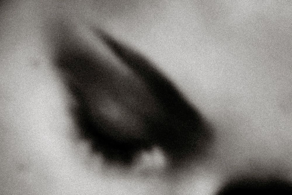 Close-up black and white abstract image of a dark eye socket, blurred and grainy.