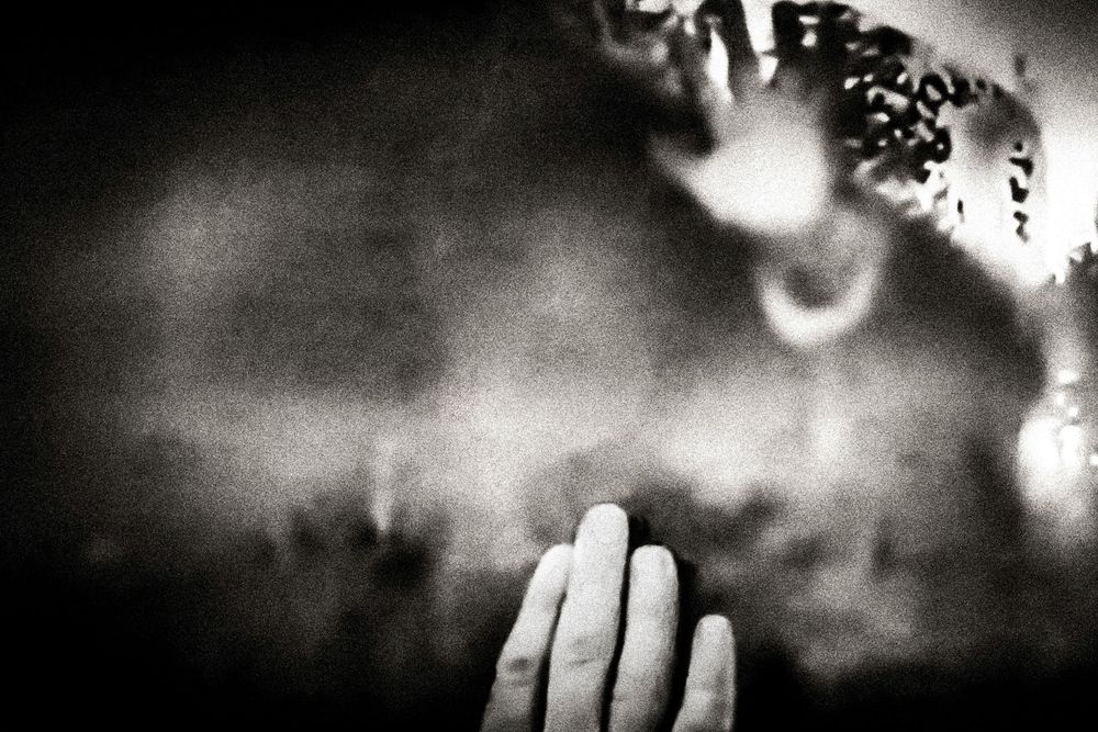 Black and white photo of hands pressed together in prayer against a dark, ethereal background.