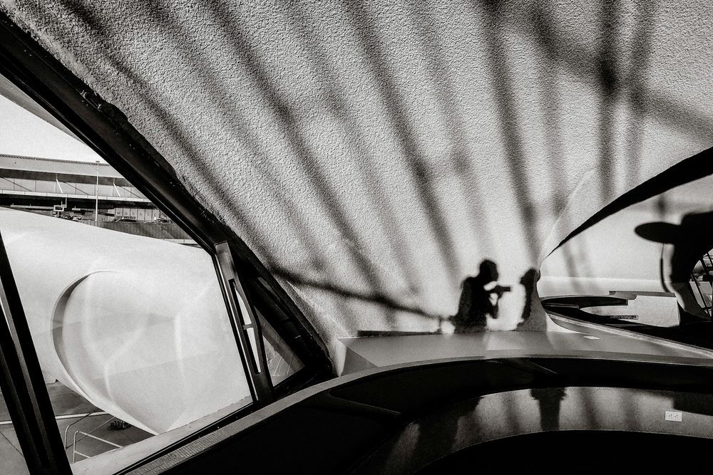 Black and white photo of a car interior with blurred silhouettes of people visible through a textured window.
