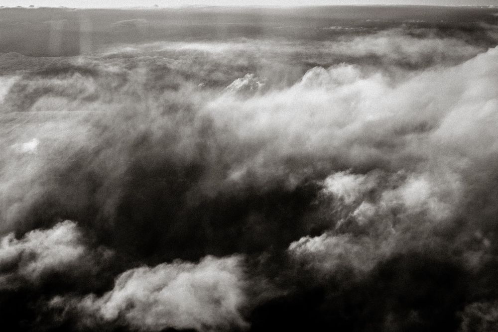 Black and white aerial photo of dramatic cloud formations rolling over a vast landscape below.