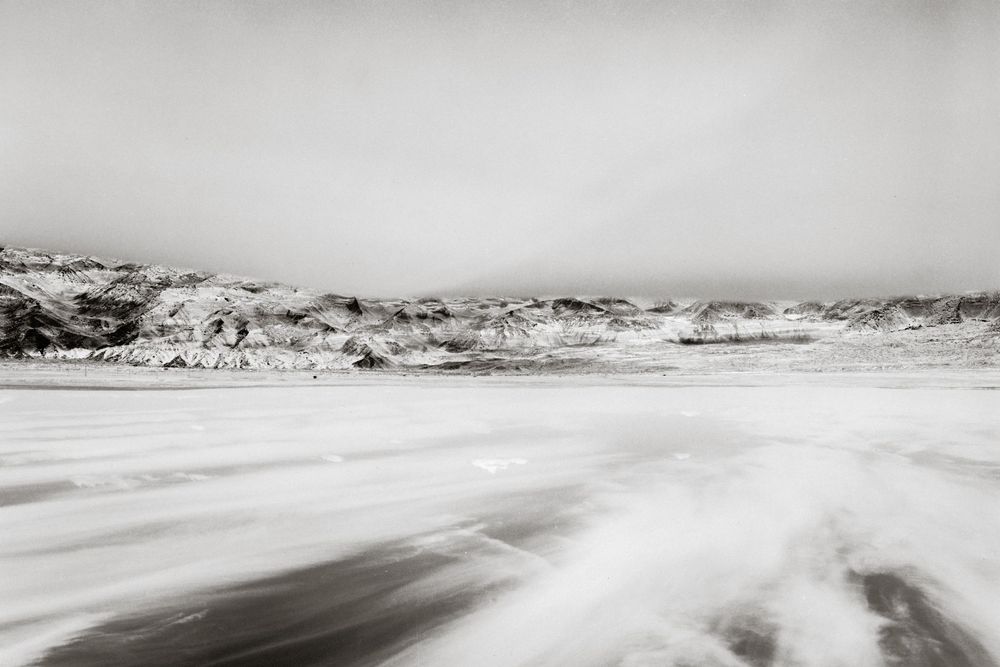 Black and white long exposure photo of ocean waves crashing on a beach with rocky cliffs in the background.