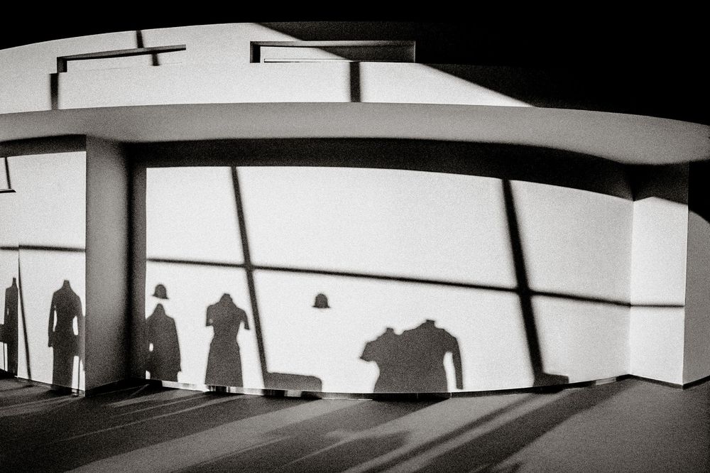 Black and white photo of three shadowy silhouettes cast on a curved white building wall at night.