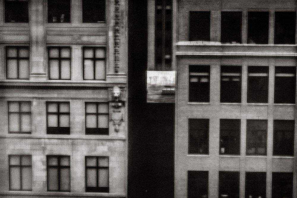 Black and white urban photography of classic multi-story buildings with large windows in a dense city landscape.