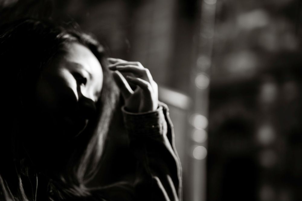 Black and white photo of a woman with her hand raised to her face, looking down pensively.