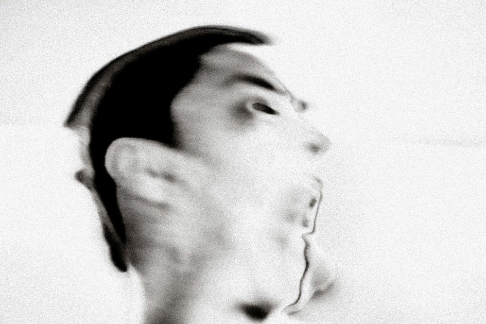 Blurred black and white portrait of a man's face in motion, creating an abstract double-exposure effect.