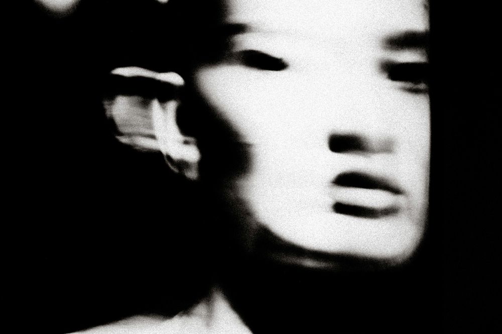 Blurred black and white portrait of a face with motion blur effect creating an ethereal, ghostly appearance.