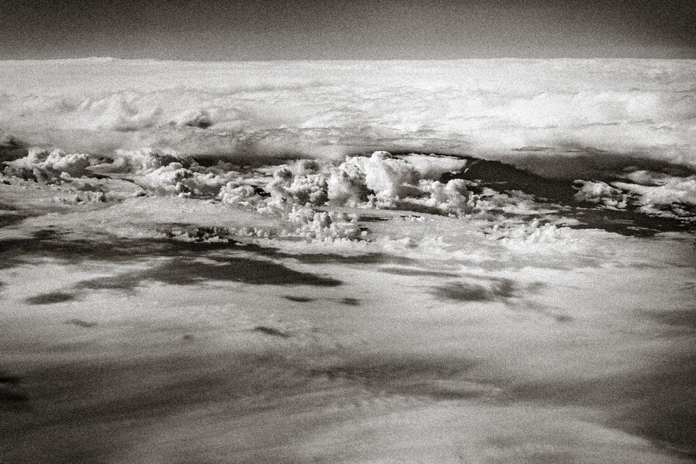 Black and white aerial photograph of dramatic cloud formations over Earth's surface viewed from high altitude.