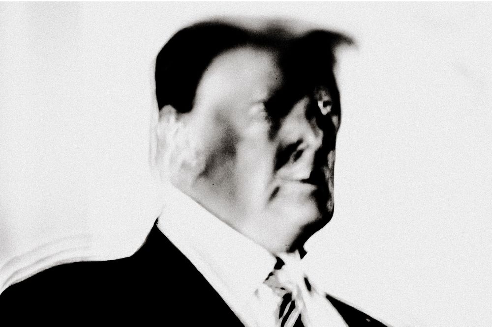 Black and white portrait of a man in a suit and tie, shot from a low angle with dramatic lighting.