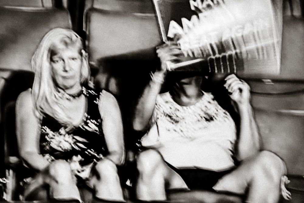 Black and white photo of two women seated at an event, one holding a Make America Great Again sign.