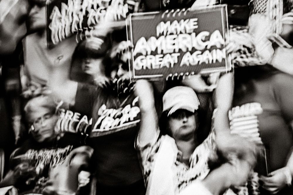Black and white photo of crowd at political rally holding Make America Great Again signs.