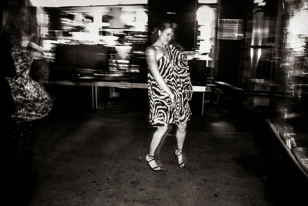 Black and white photo of a woman in a zebra print dress and heels dancing on a city sidewalk at night.