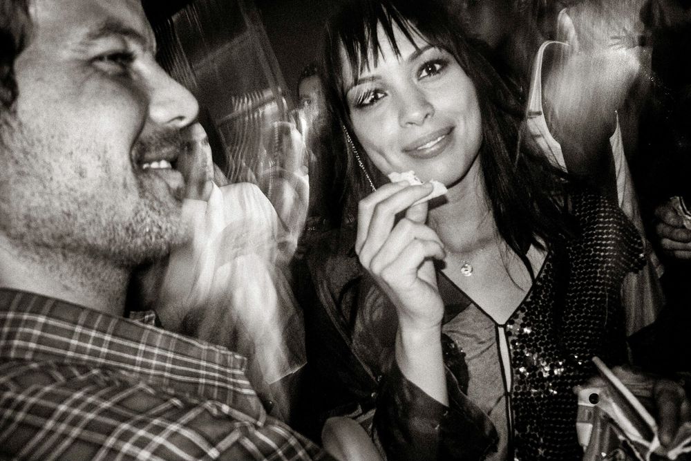 Black and white photo of a smiling man and woman enjoying a lively social gathering or party event.