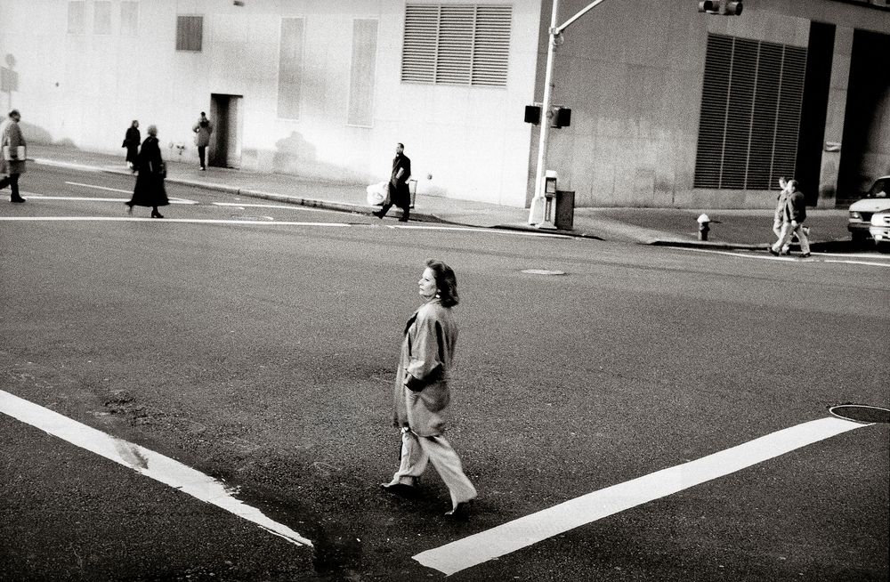Black and white photo of pedestrians crossing a wide urban street intersection in a city.